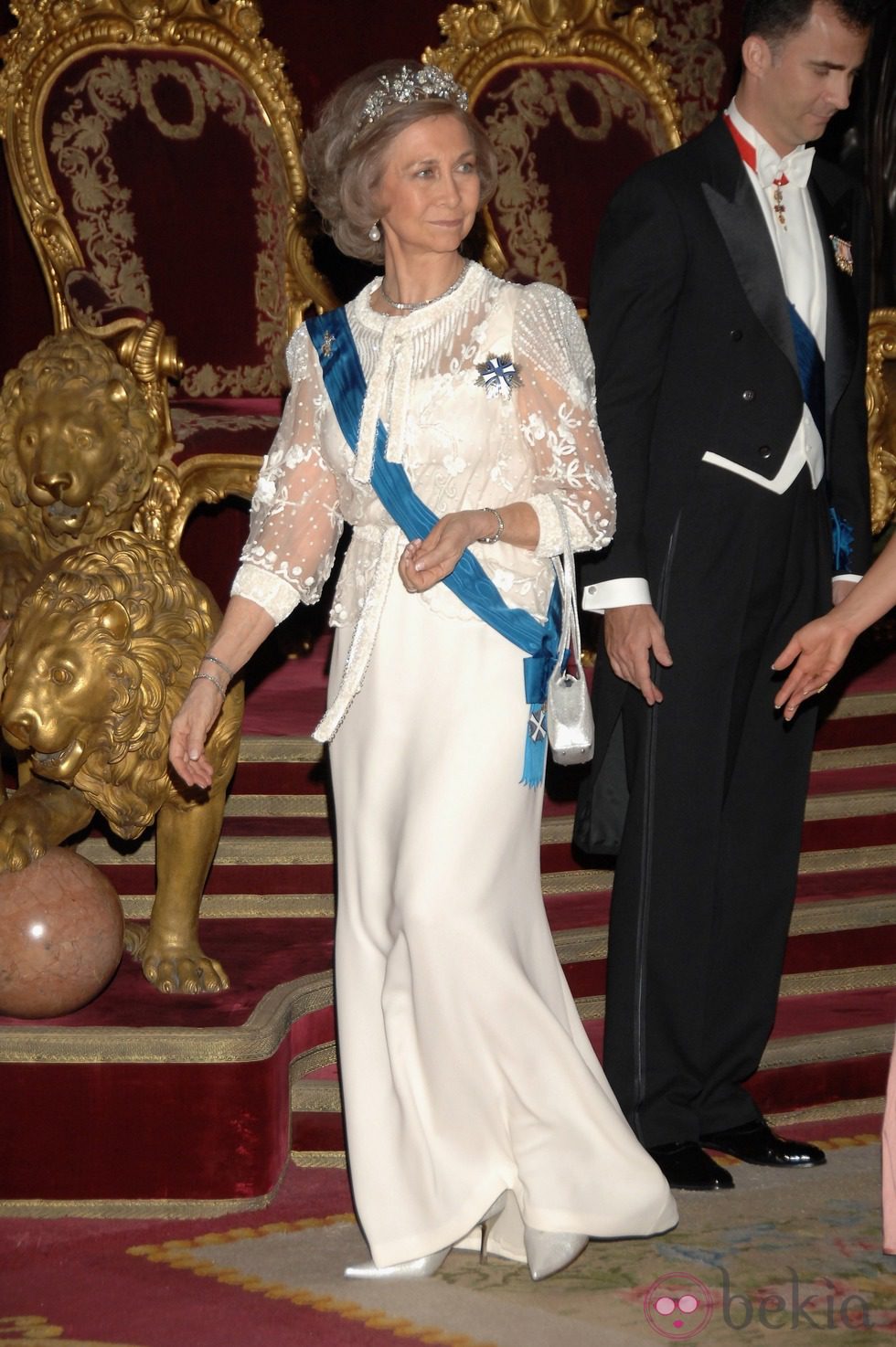 Look de la reina Sofía con vestido de gala largo en color blanco roto y mangas transparentes con detalles florales en relieve 