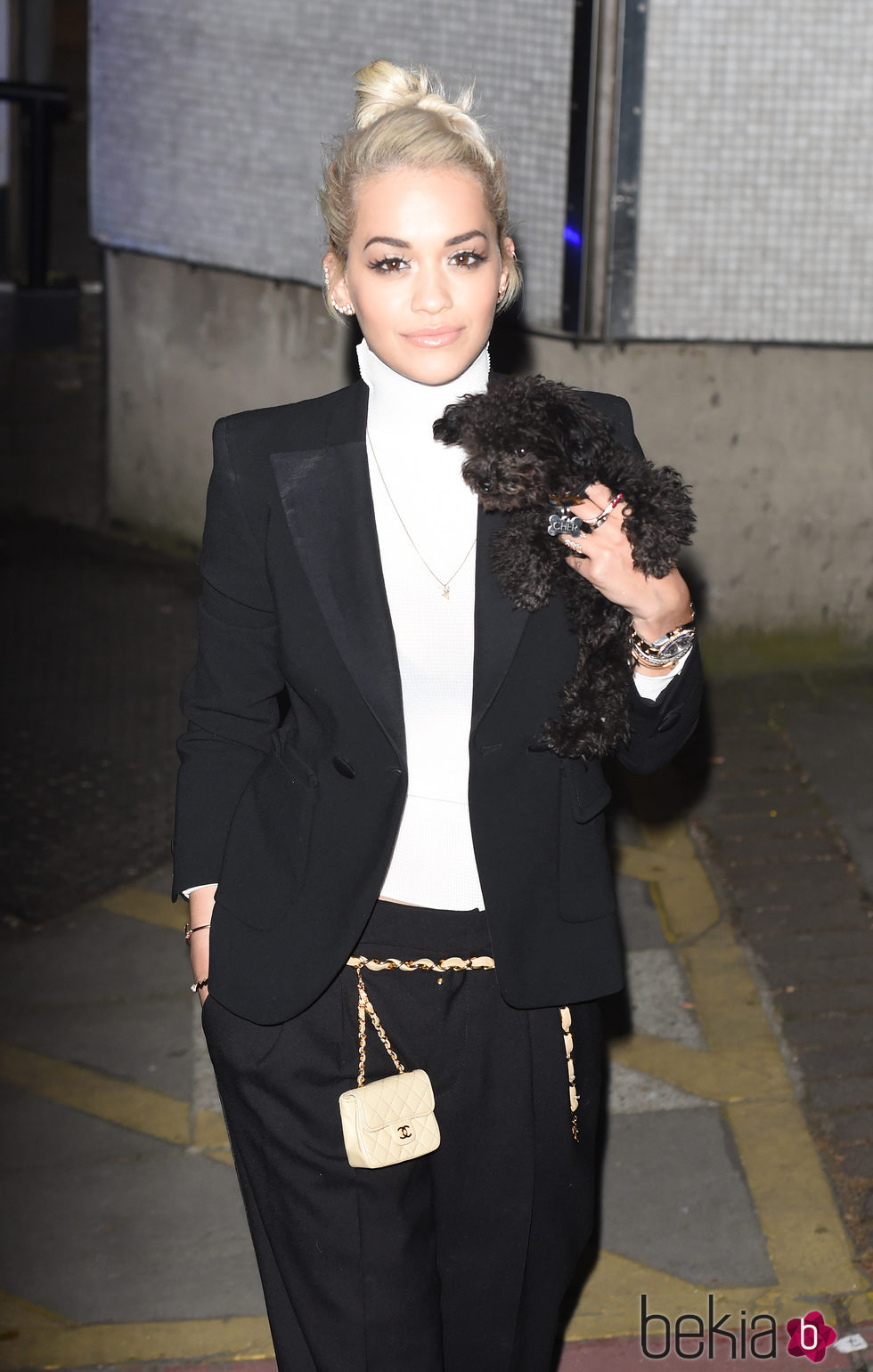 Rita Ora con traje negro, camiseta blanca básica y su perro a modo de complemento